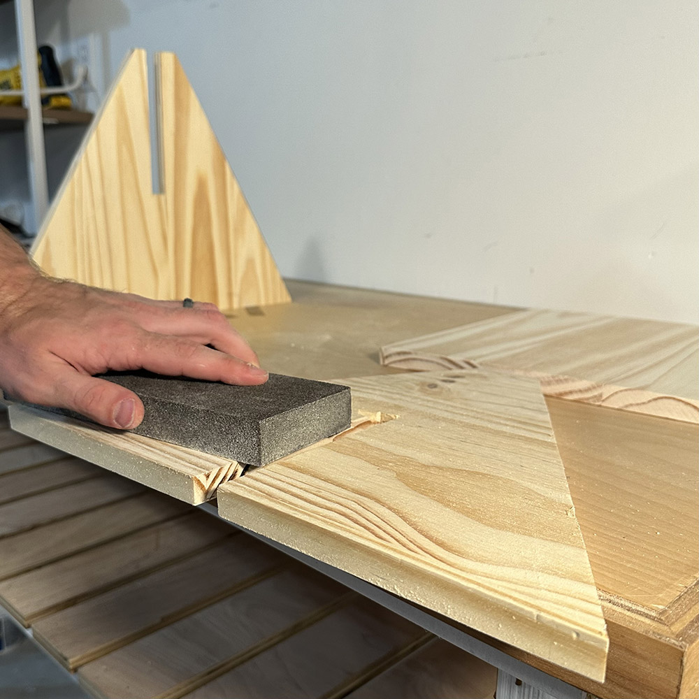 A man sanding a wooden plank down with a sanding sponge.