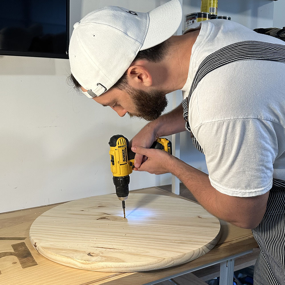 A man drilling into the center of a wooden circle.