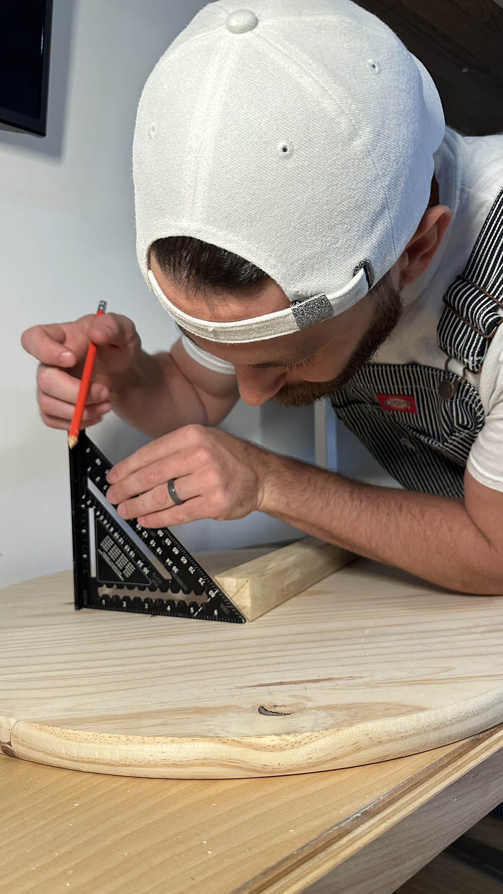 A man using a ruler to measure a wooden plank.