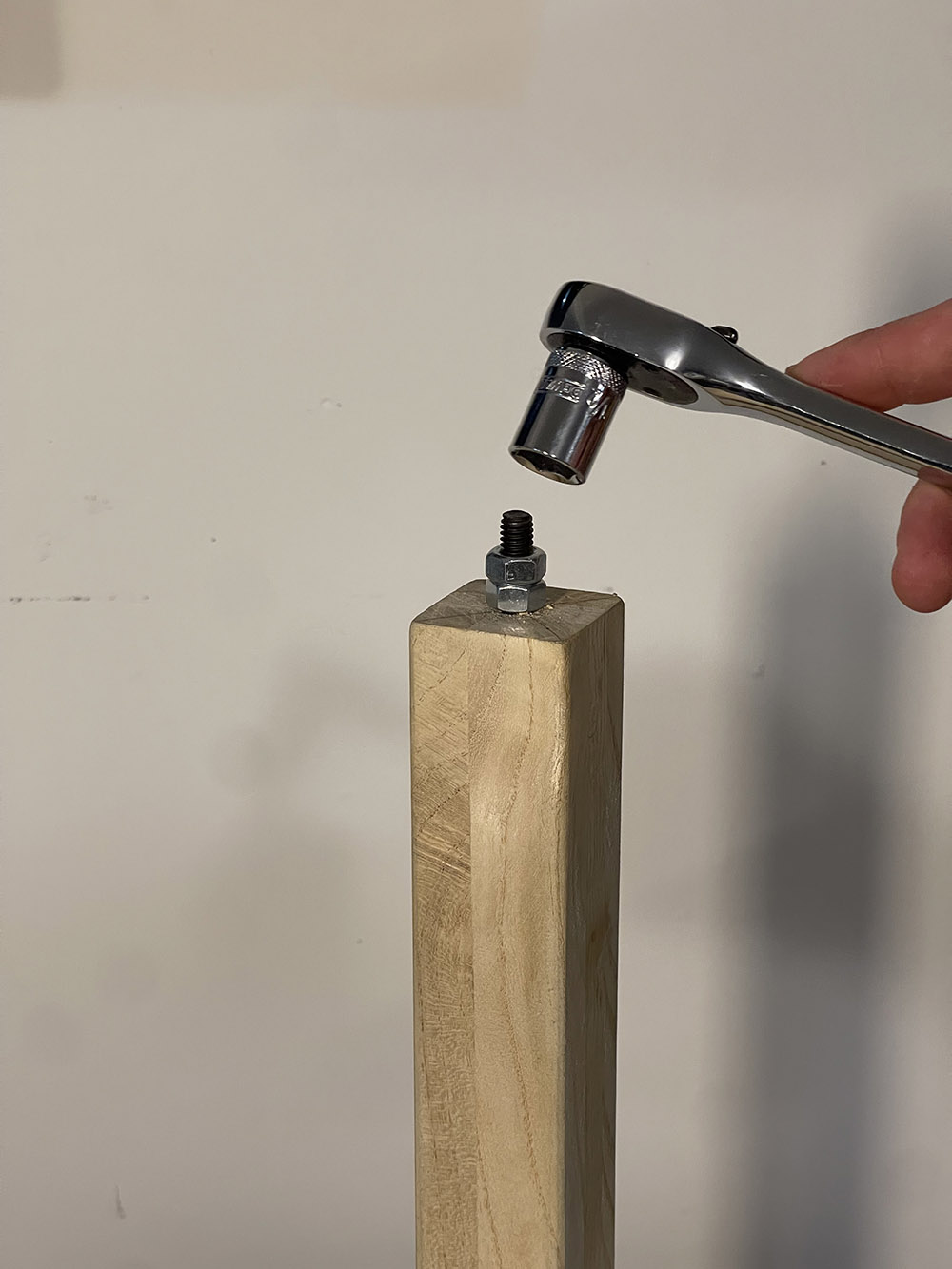 Someone holding a wrench next to a hanger bolt fastened to a wooden plank.