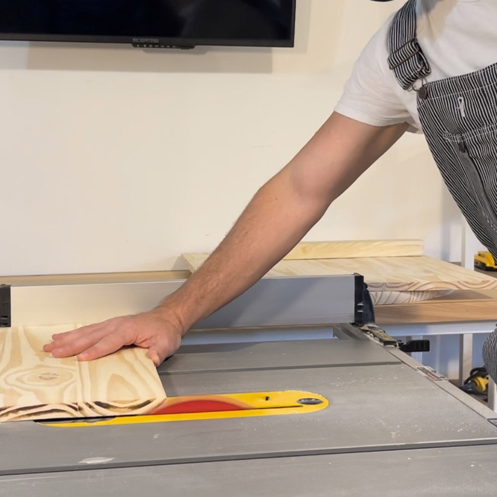 A man cutting a piece of wood with a table saw.