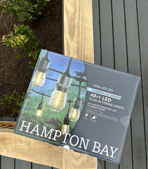 A box of Hampton Bay outdoor lights sitting on the deck railing.
