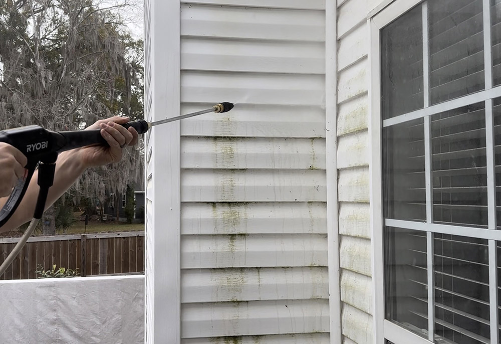 A man spraying the side of a wall with an electric pressure washer.