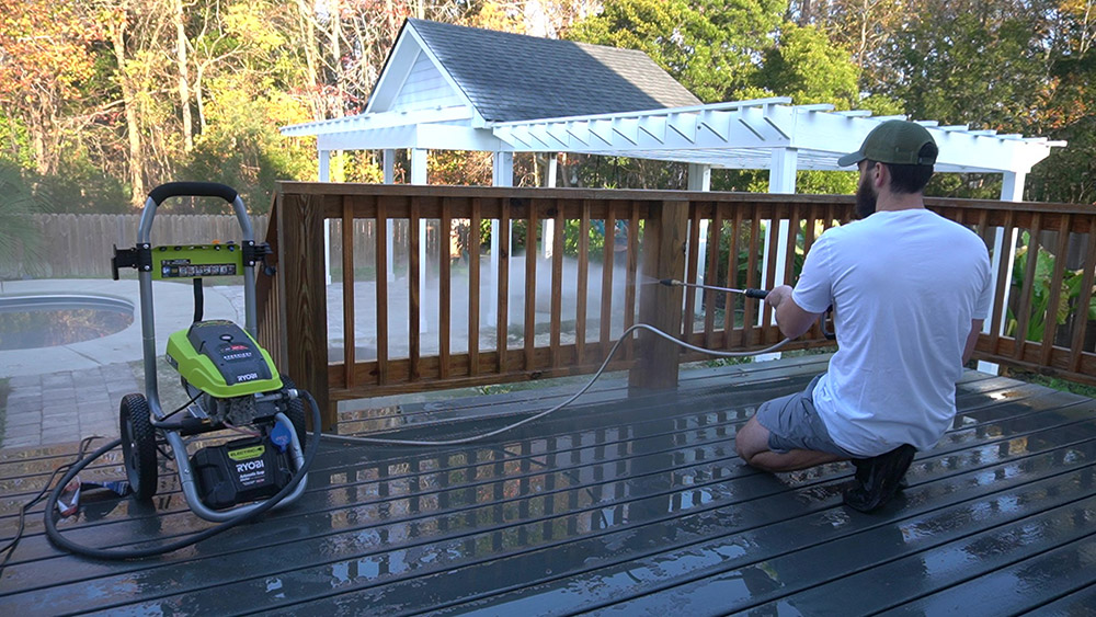 A man spraying a patio deck floor with an electric pressure washer.