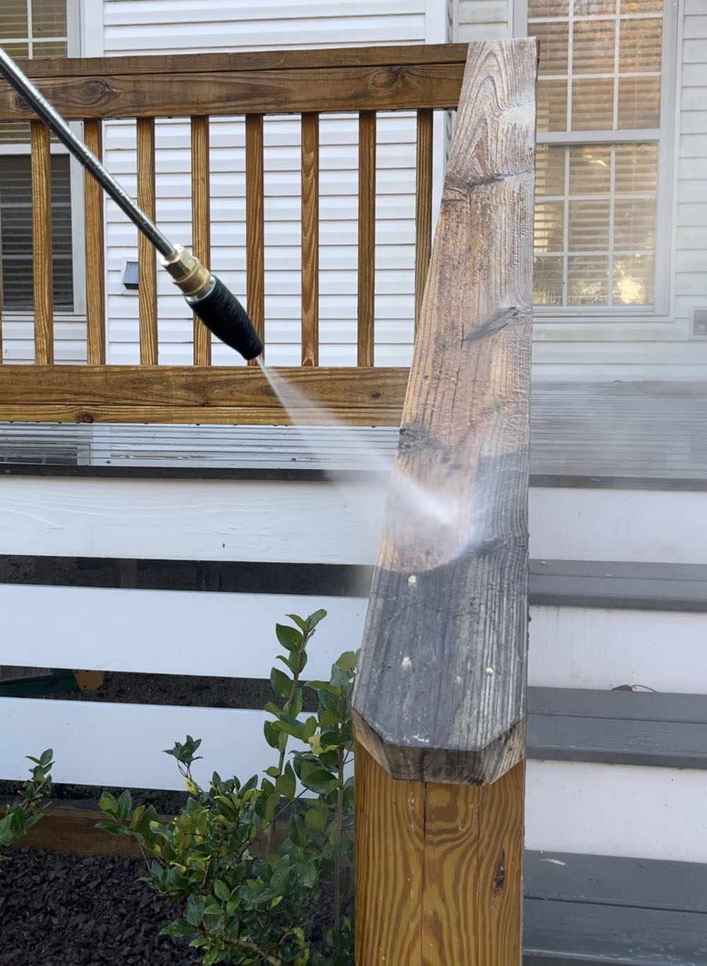 A man spraying the railing on a deck with an electric pressure washer.