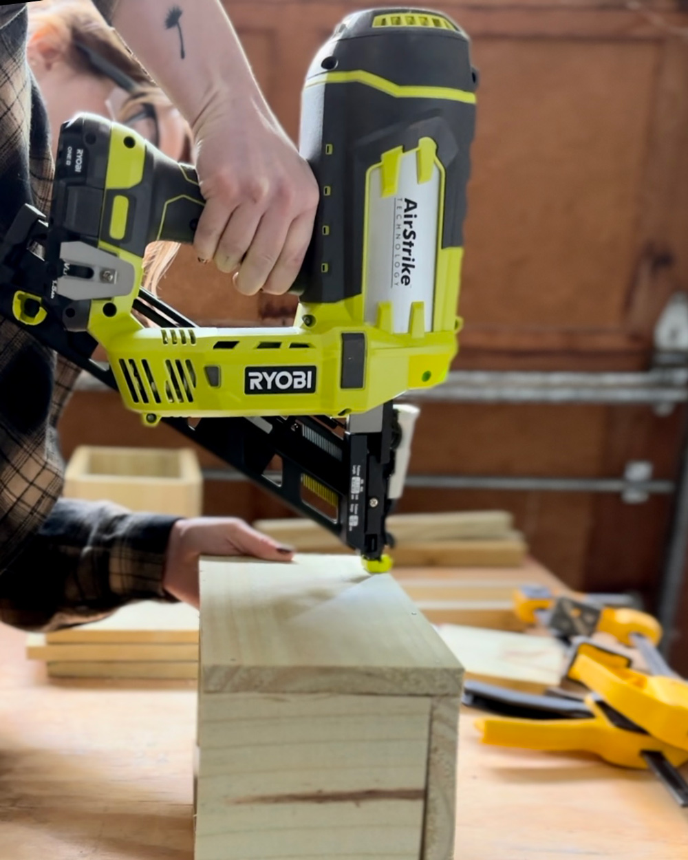 A woman using a Ryobi nailer to assemble wood planks. A woman using a Ryobi nailer to assemble wood planks.
