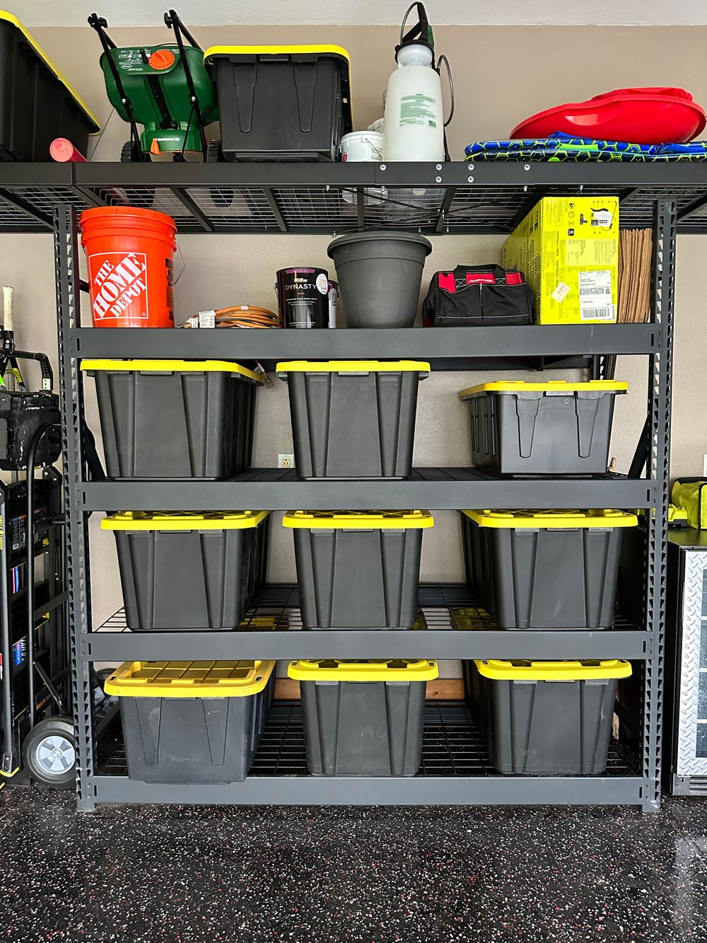A shelving unit with storage totes, a Homer bucket, and other miscellaneous items.