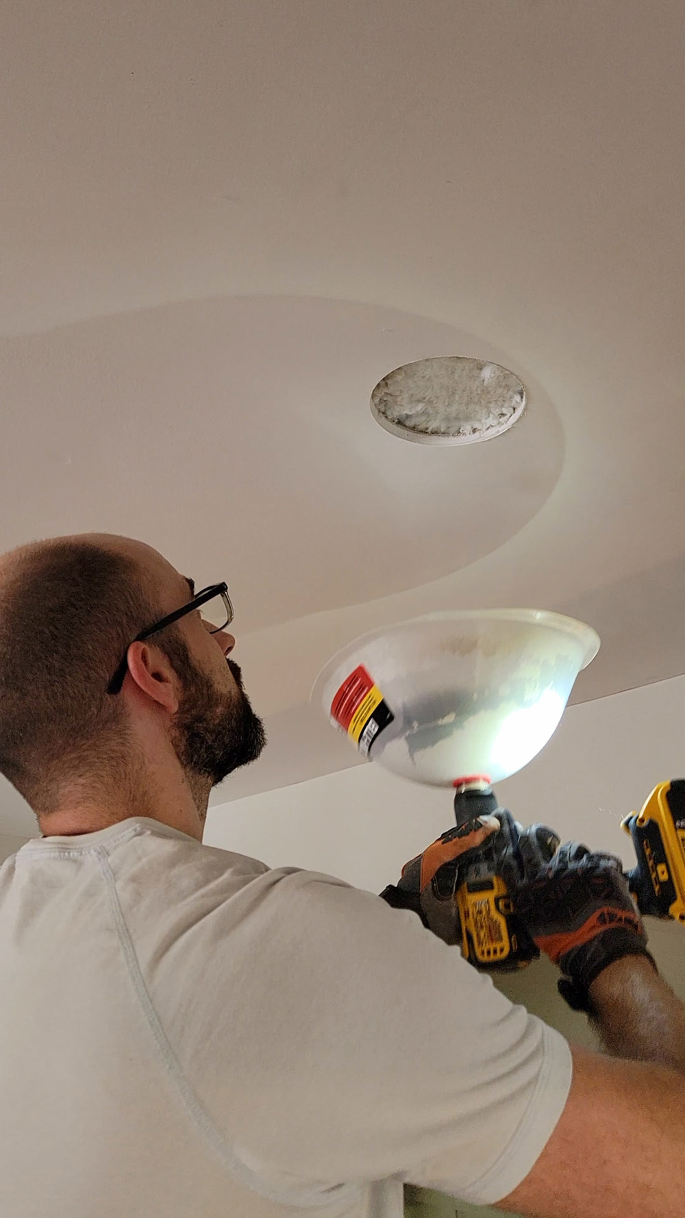 Man placing light fixture on to ceiling. 