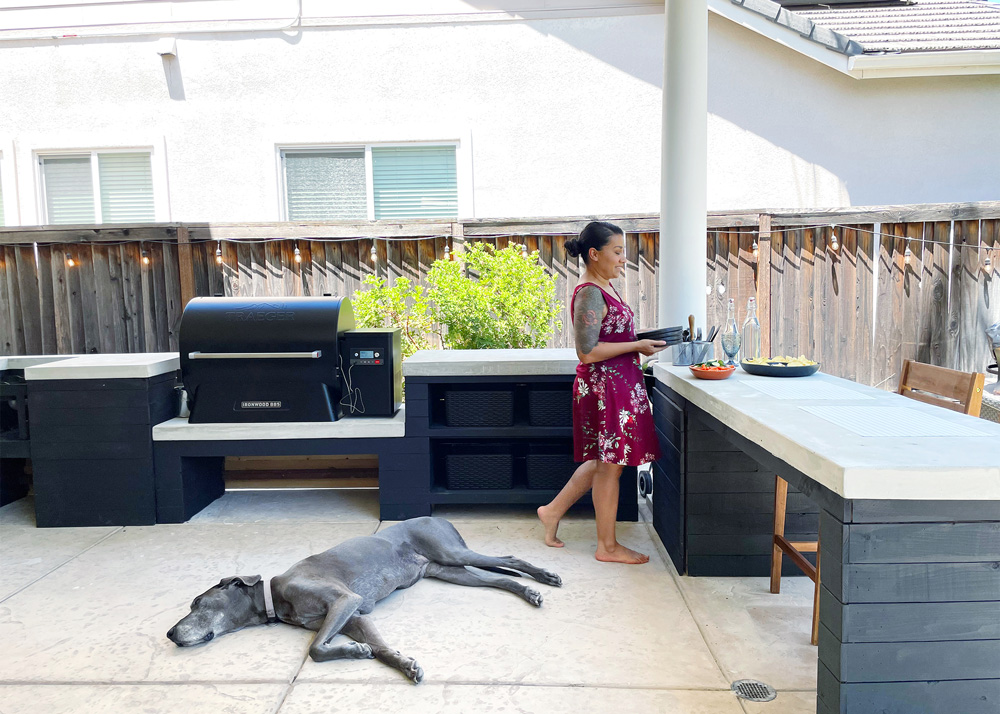 Woman standing in the corner of an outdoor patio area with a large grey dog laying in the center of the patio