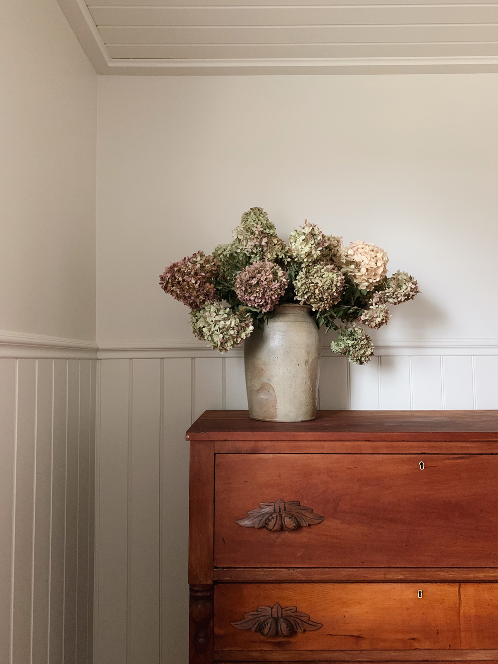 The oiled wooden dresser with a set of potted flowers sitting atop it.