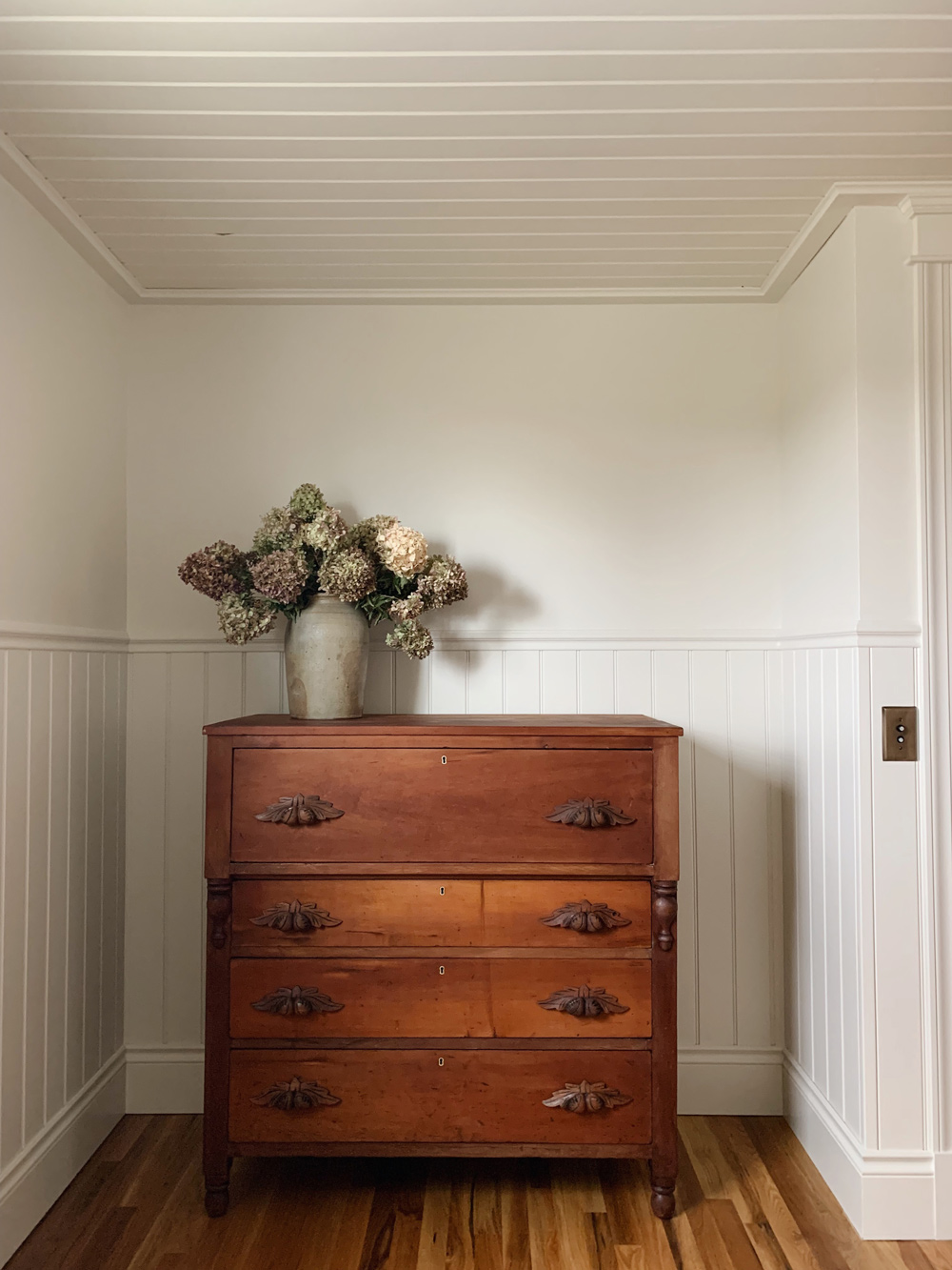 A wide shot of the wooden dresser and vase.