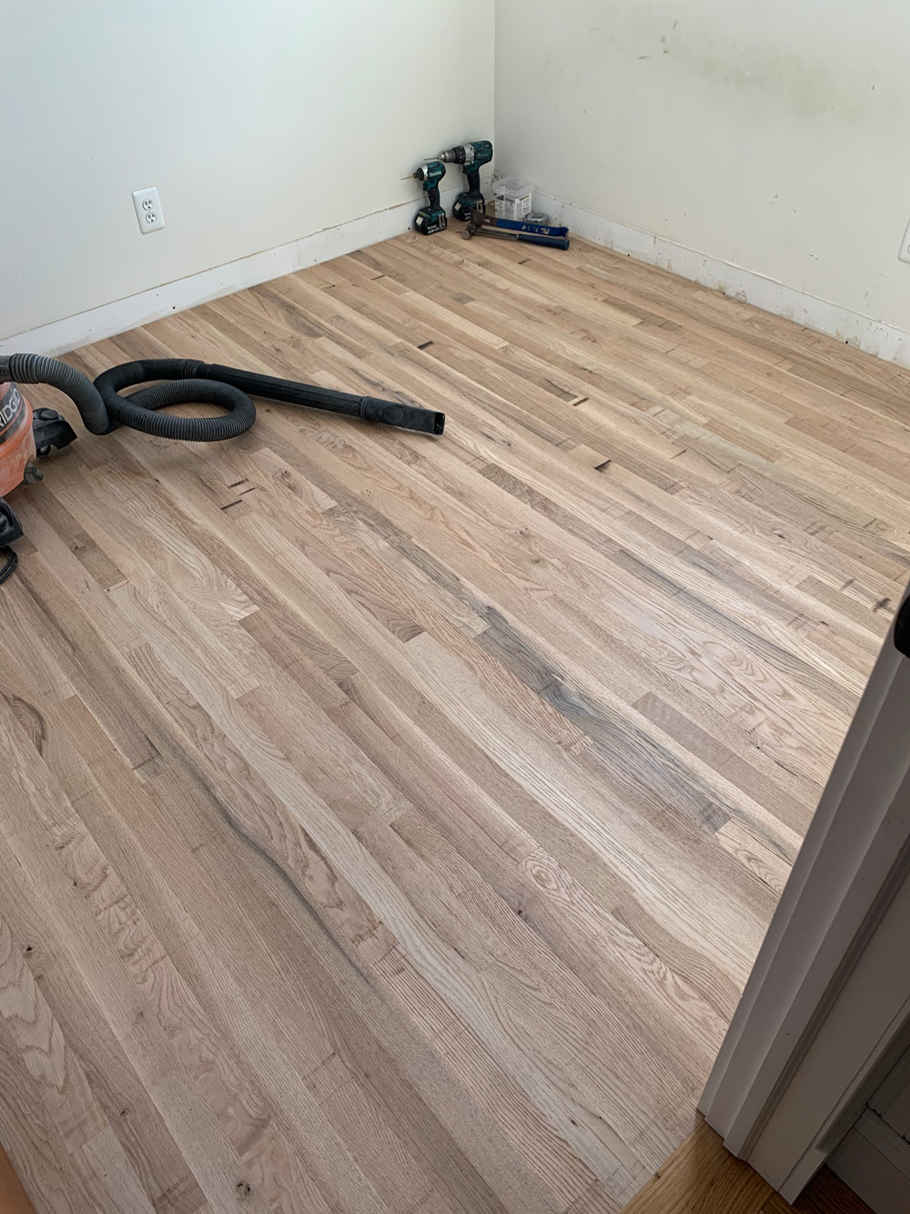 Wood floor with a set of drills and a vacuum sitting atop it.