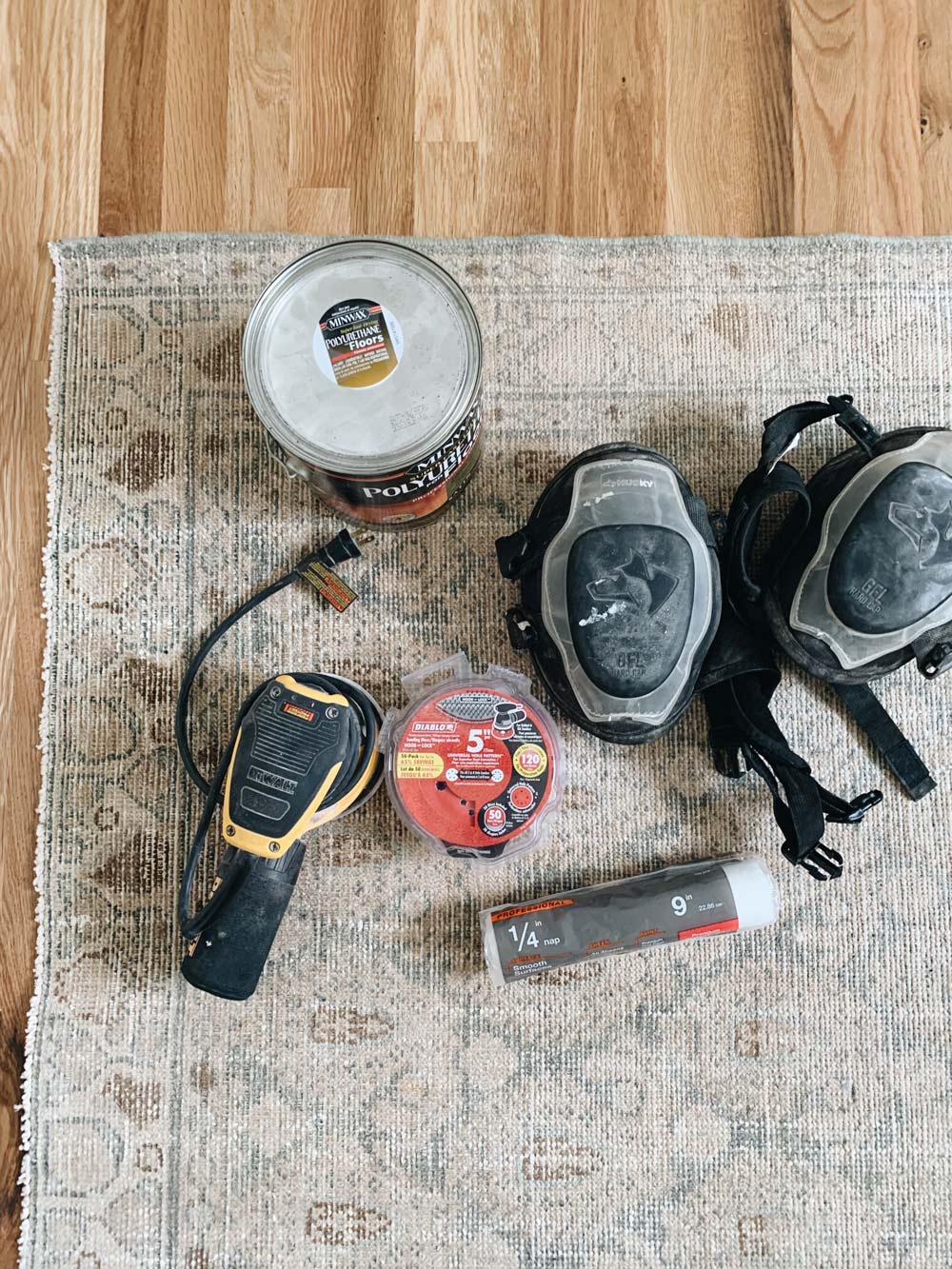 A set of tools, nails, a bucket of paint, and a sander sitting on a carpet.