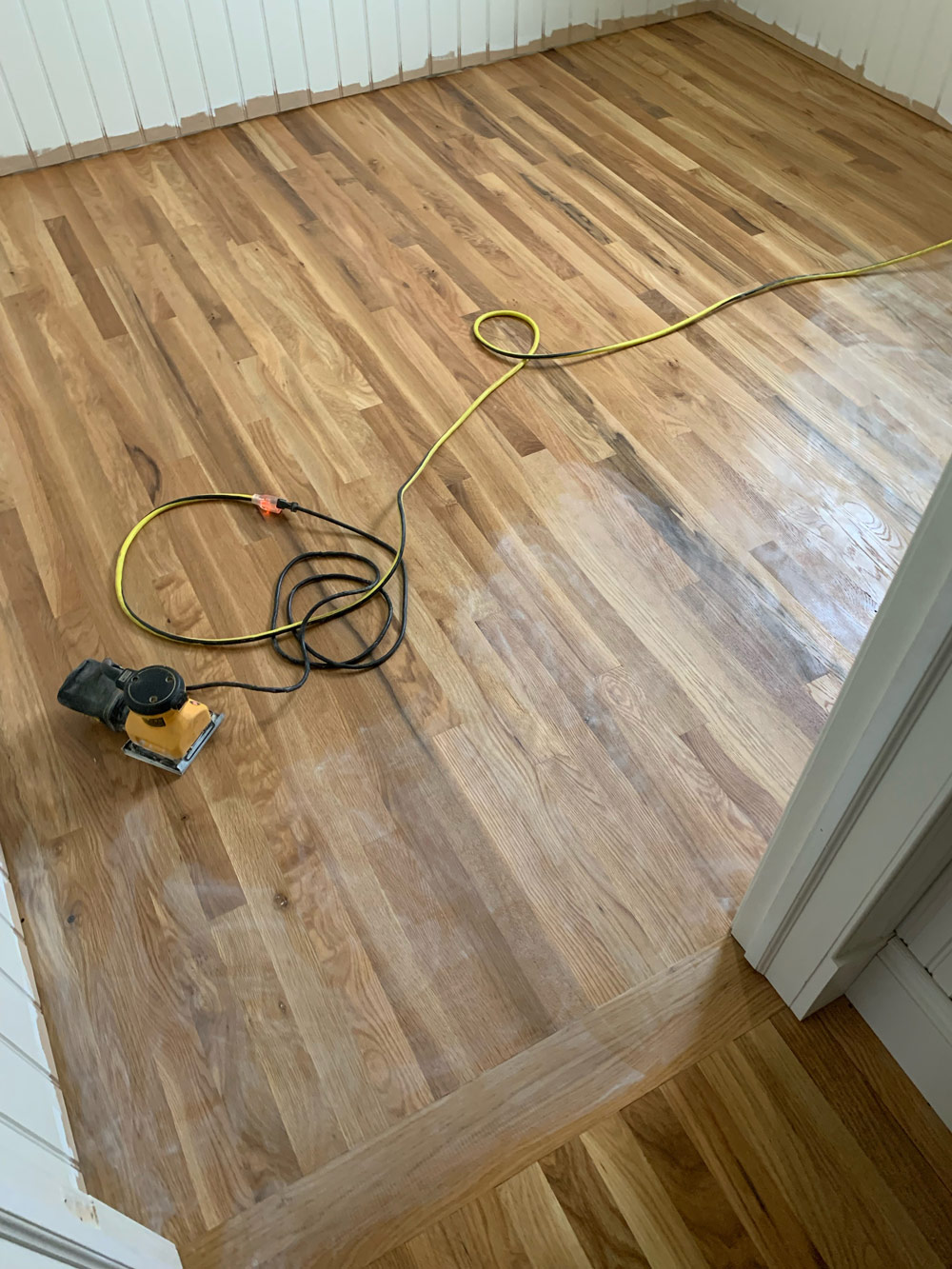 A recently sanded wooden bedroom floor, with an electric sander sitting atop.