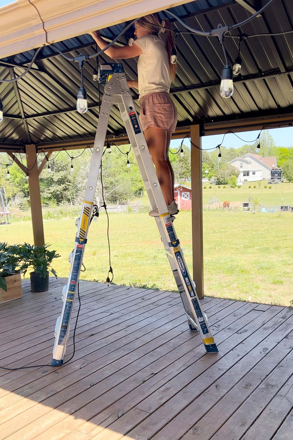 Woman standing on a ladder hanging string lights. Woman standing on a ladder hanging string lights.