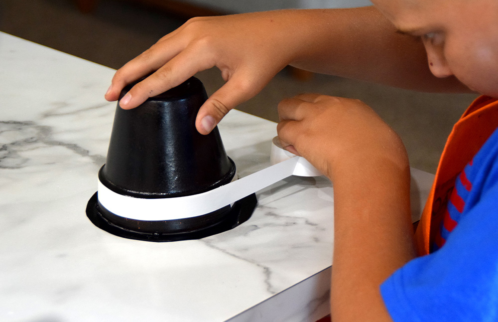 A child applying electrical tape around the brim of the hat.
