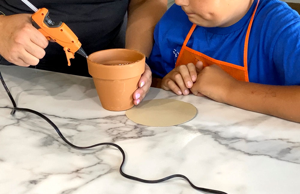 Hand applying hot glue to the top of a flower pot.