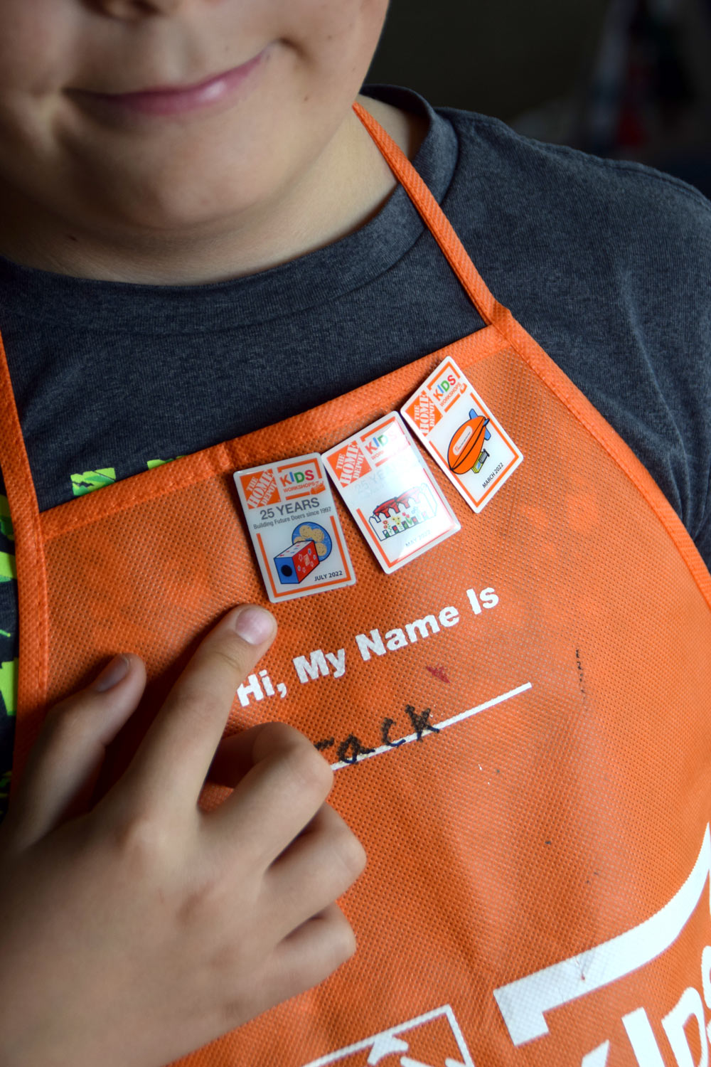Boy with a Home Depot apron pointing to a certification pin.