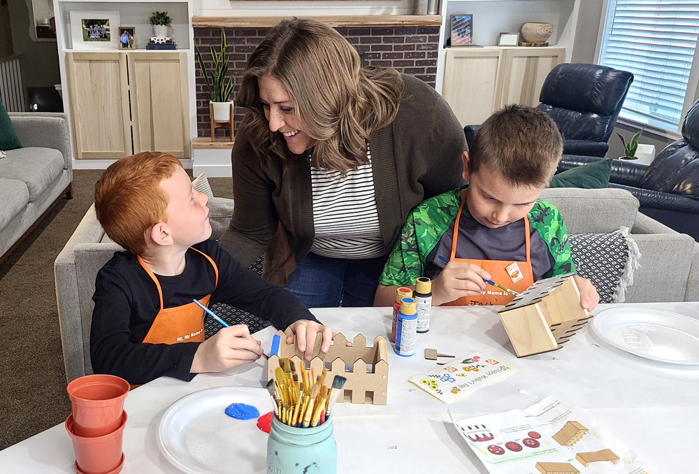 A woman helping two boys as they paint an assembled Picket Fence Planter.
