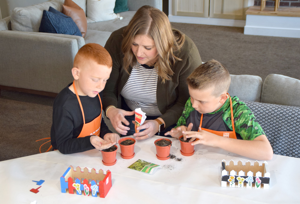 A woman helping two boys put seeds into small pots with soil.