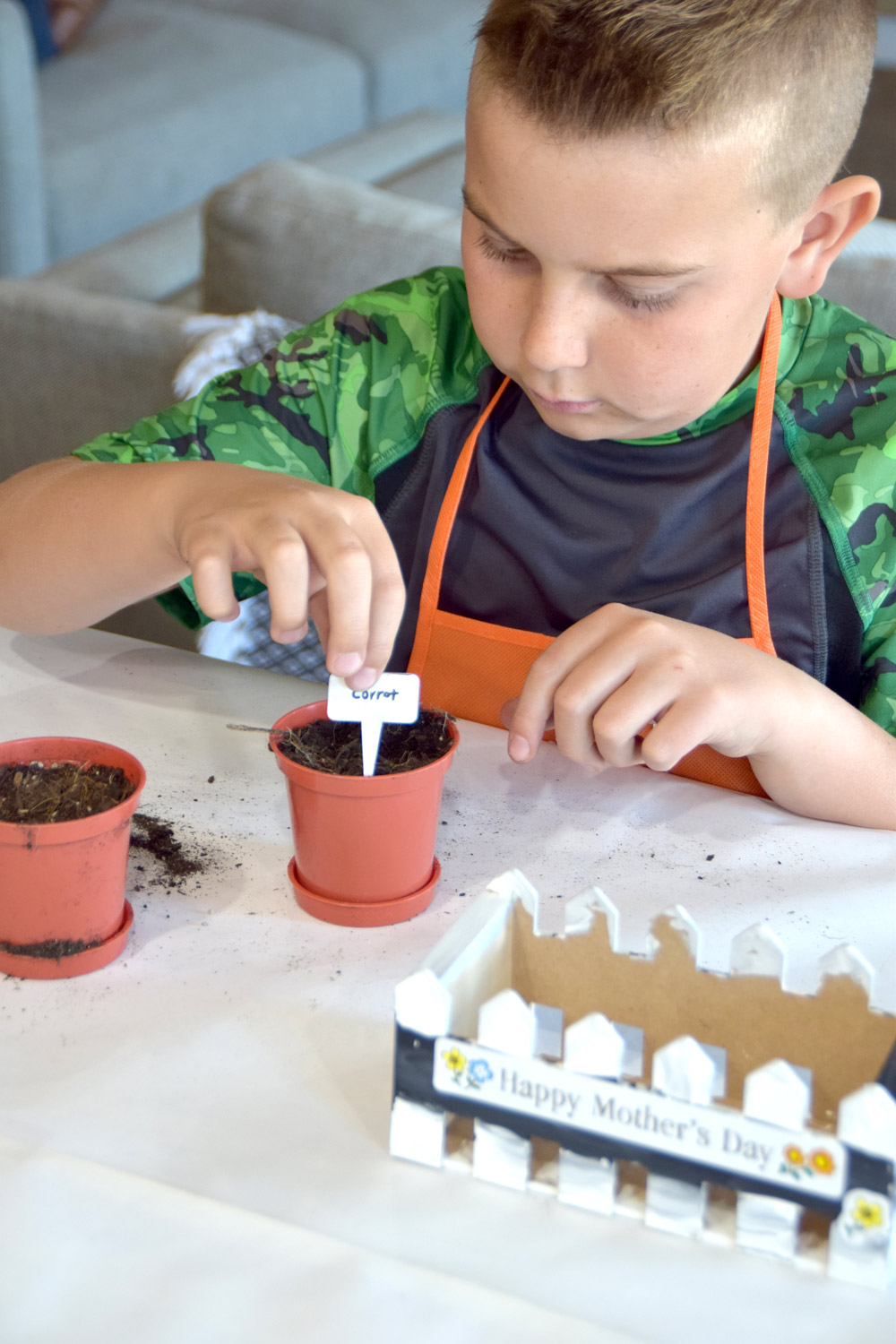 A boy placing a plant label into a small pot with soil.