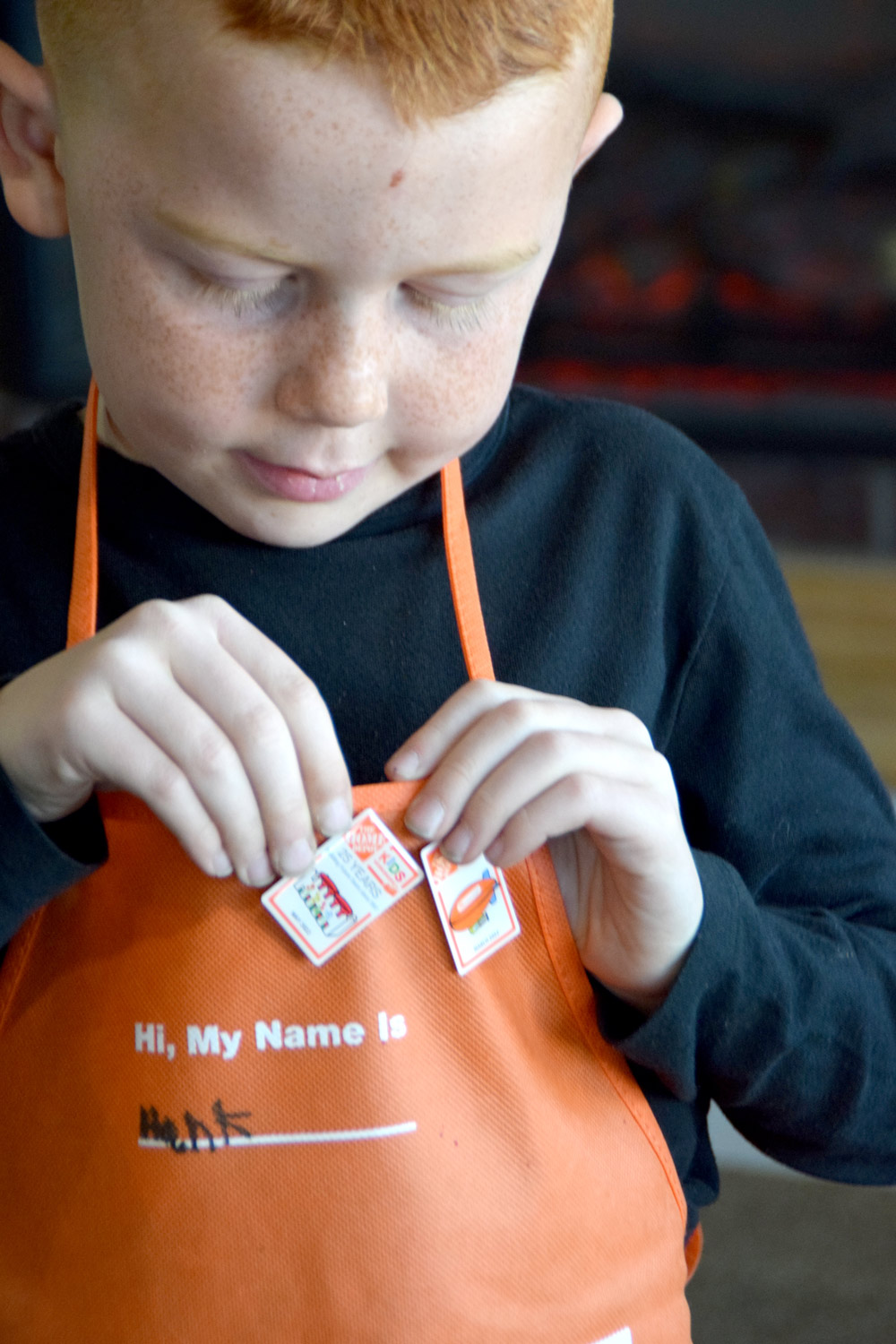 A boy pinning a Picket Fence Planter workshops planter to an orange Home Depot apron.