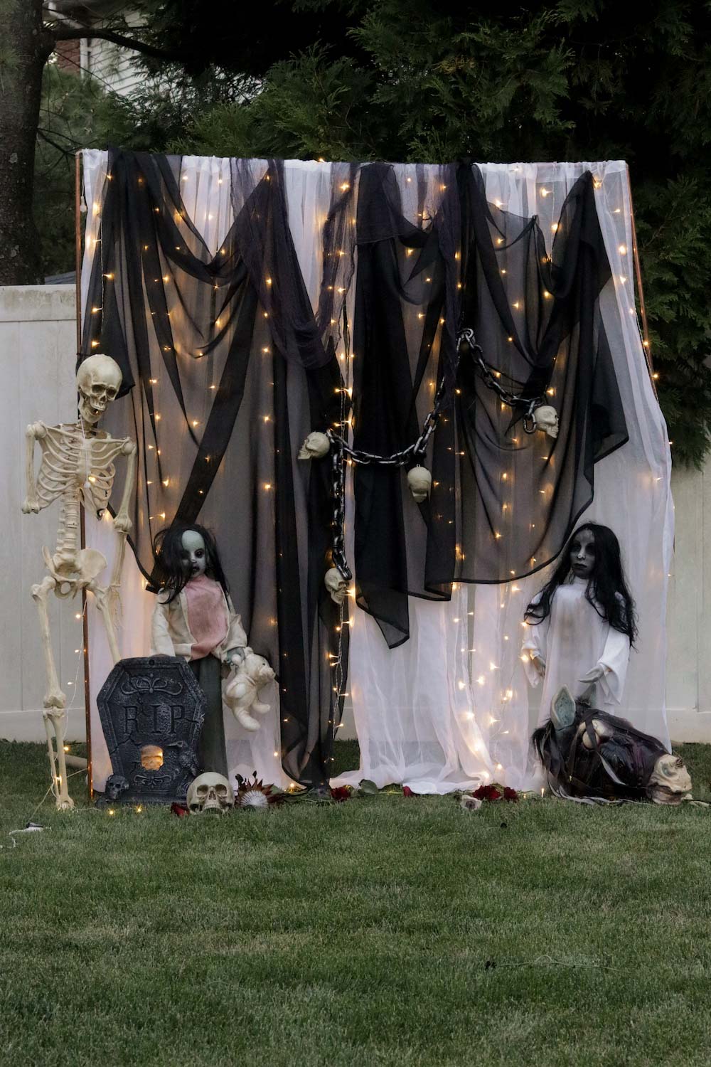 A DIY photo booth decorated with curtain lights, zombie sisters, tombstones, and skulls.