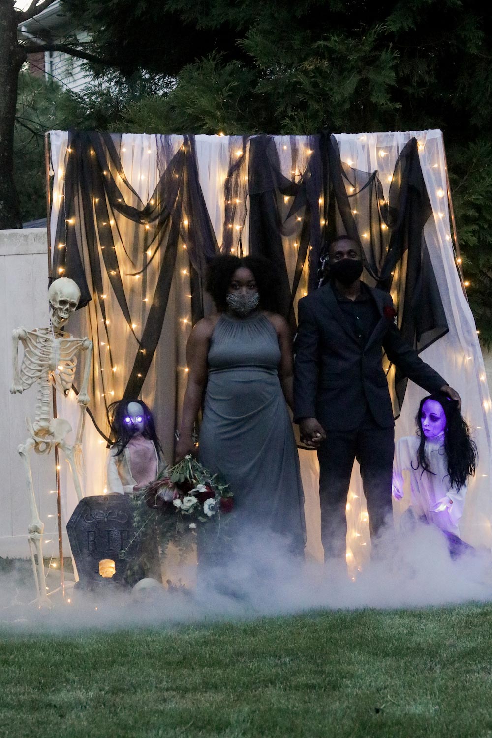 A man and woman standing in front of a DIY photo booth decorated with fog, lighting, and glowing zombie sisters.