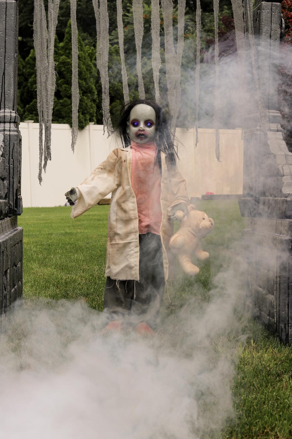 A zombie girl holding a stuffed animal in a foggy yard.
