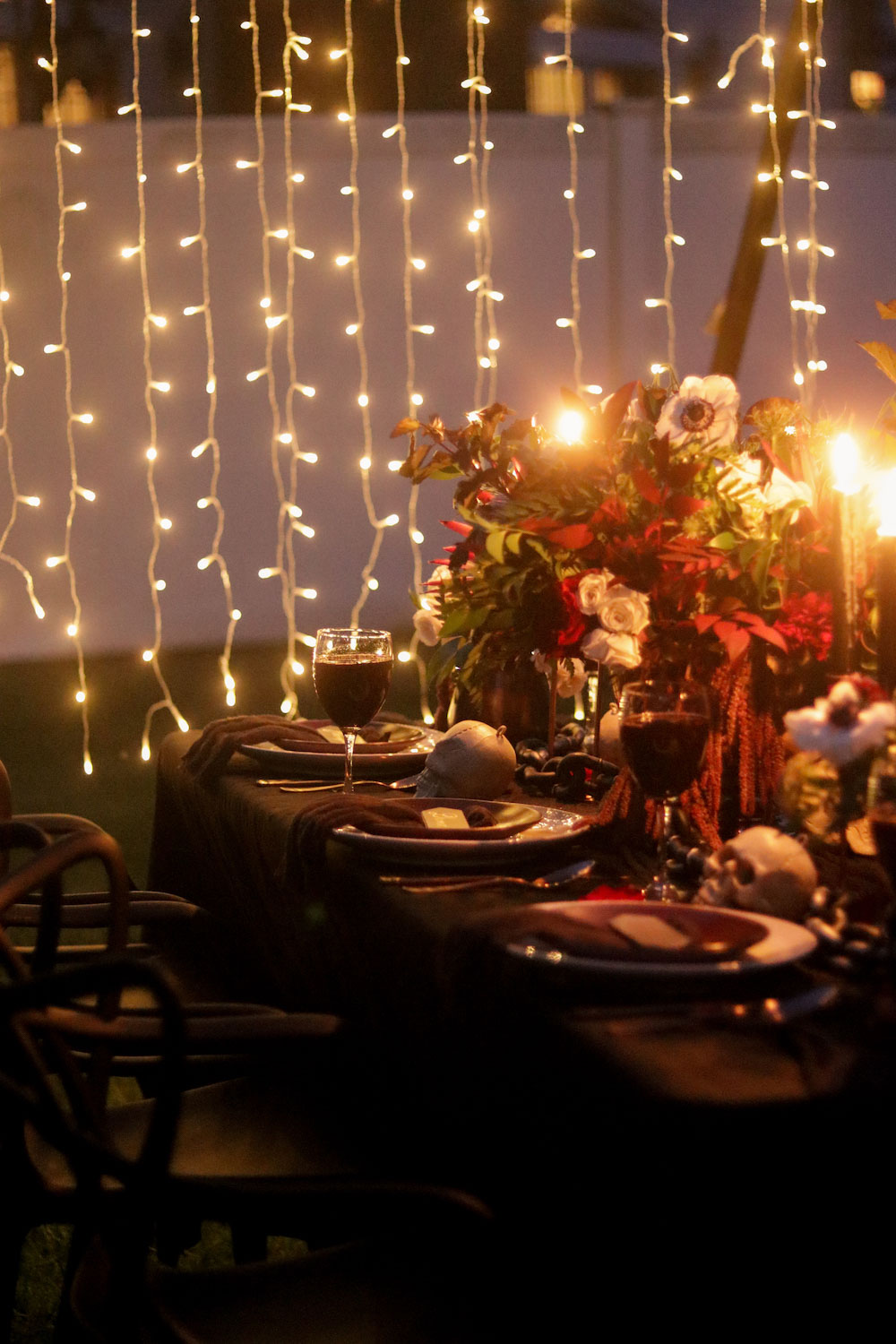 A Halloween tablescape at night lit by candles and curtain lights.