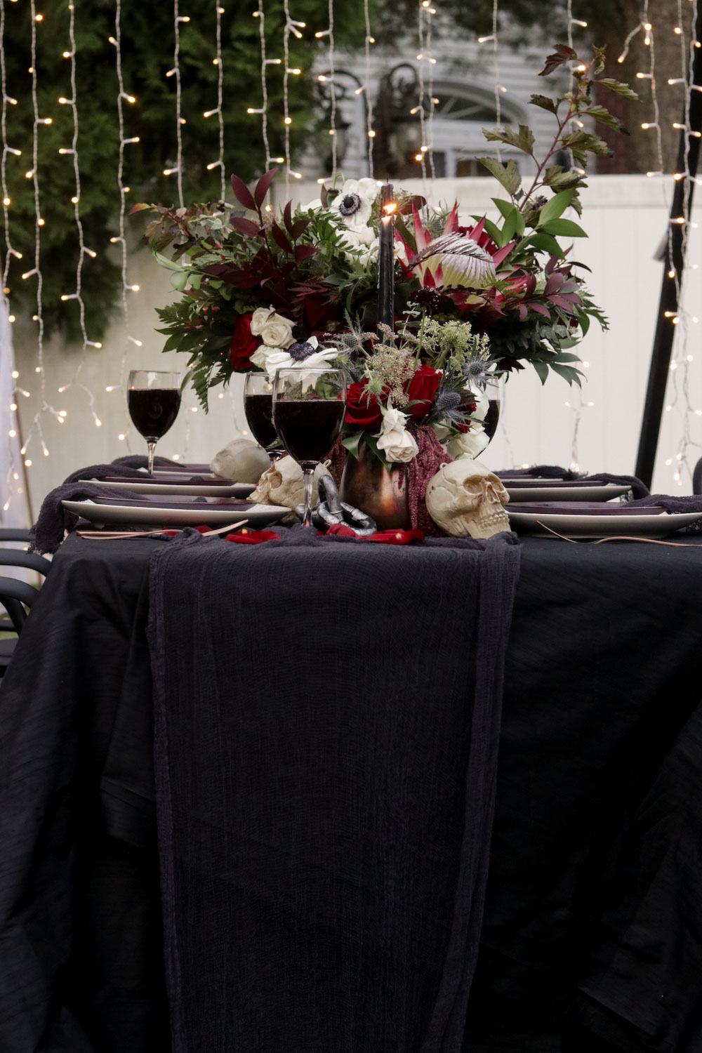 A dark colored Halloween tablescape with flowers and curtain lights.