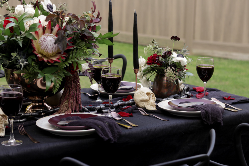 A Halloween tablescape decorated with dark linens, candles, flowers, and skulls.