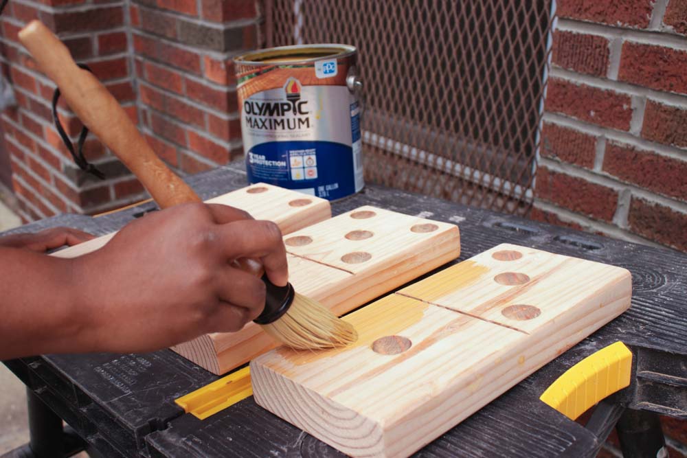 A person hand painting exterior grade sealant onto light wooden dominoes block. A person hand painting exterior grade sealant onto light wooden dominoes block.