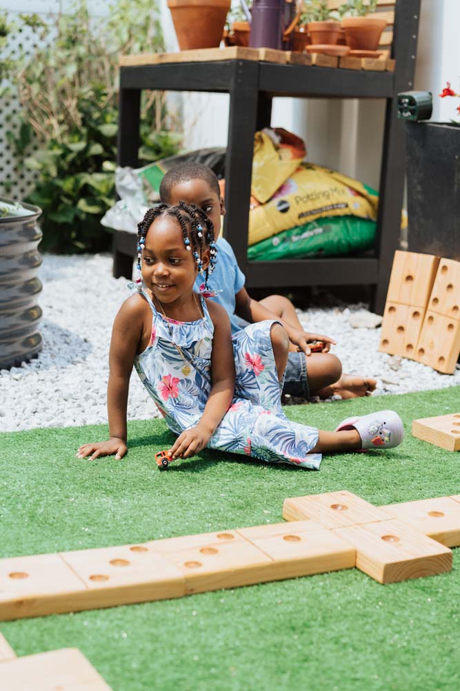 Two childen sitting on green turf near large wooden dominoes laid out for a game. Two childen sitting on green turf near large wooden dominoes laid out for a game.