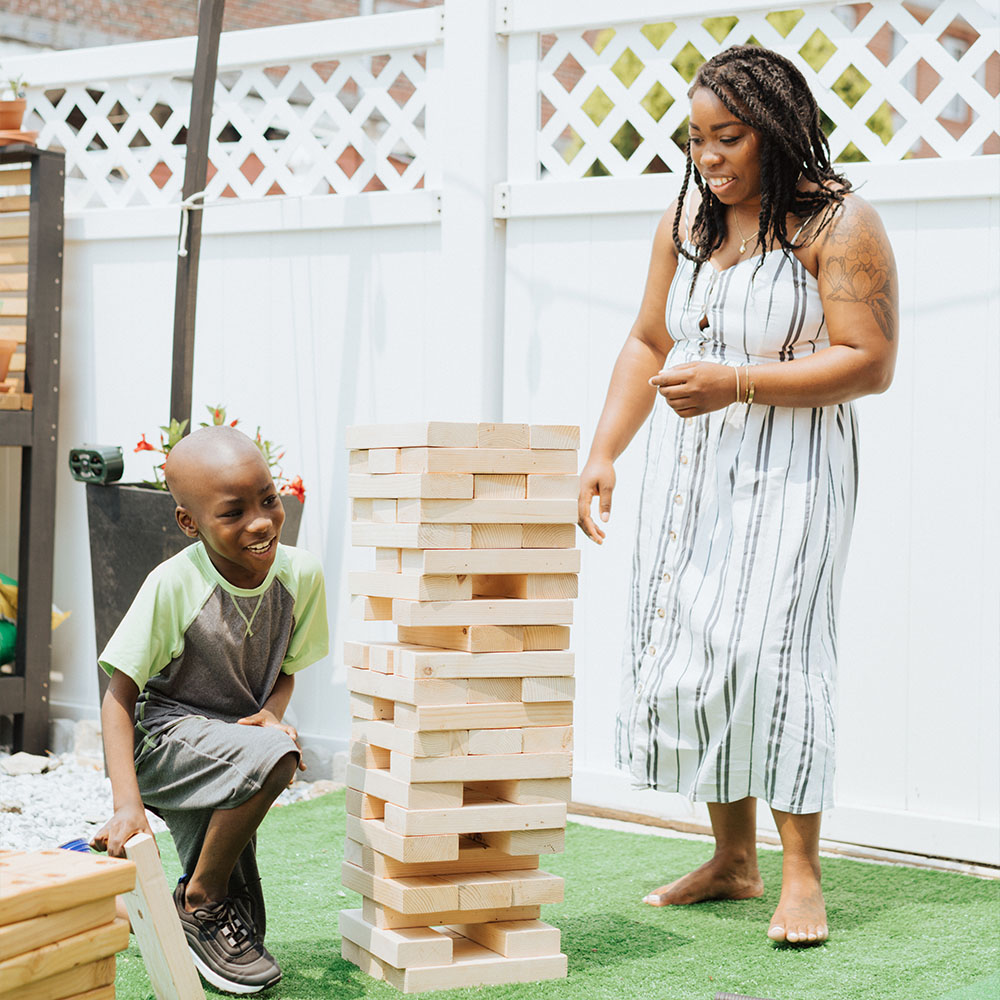 A woman and boy child standing near and playing with large wooden jenga tower. A woman and boy child standing near and playing with large wooden jenga tower.