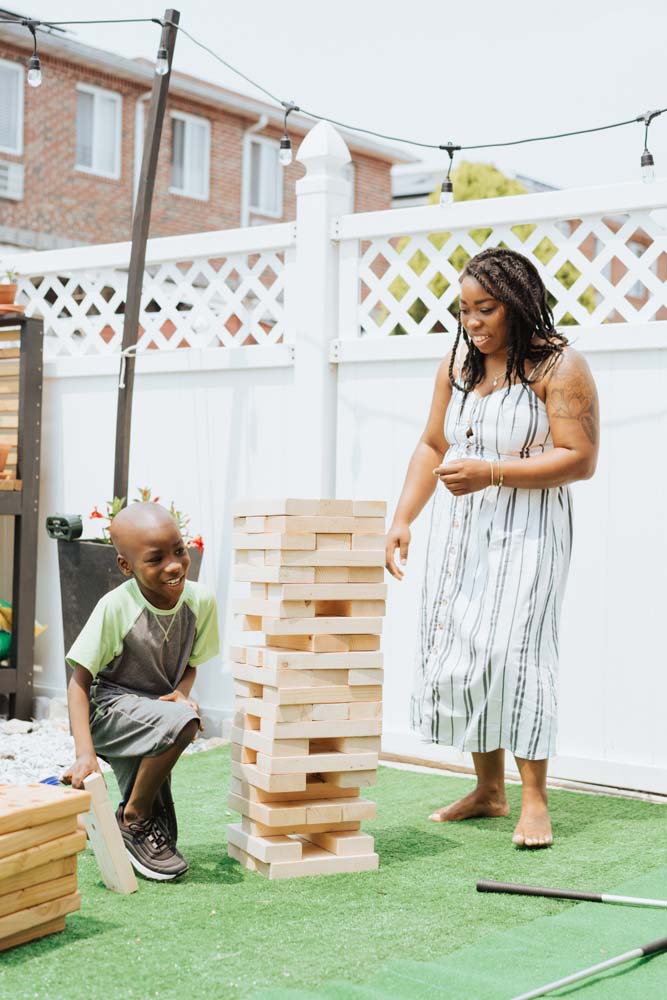 Woman and boy child standing near and playing with large wooden jenga tower. Woman and boy child standing near and playing with large wooden jenga tower.