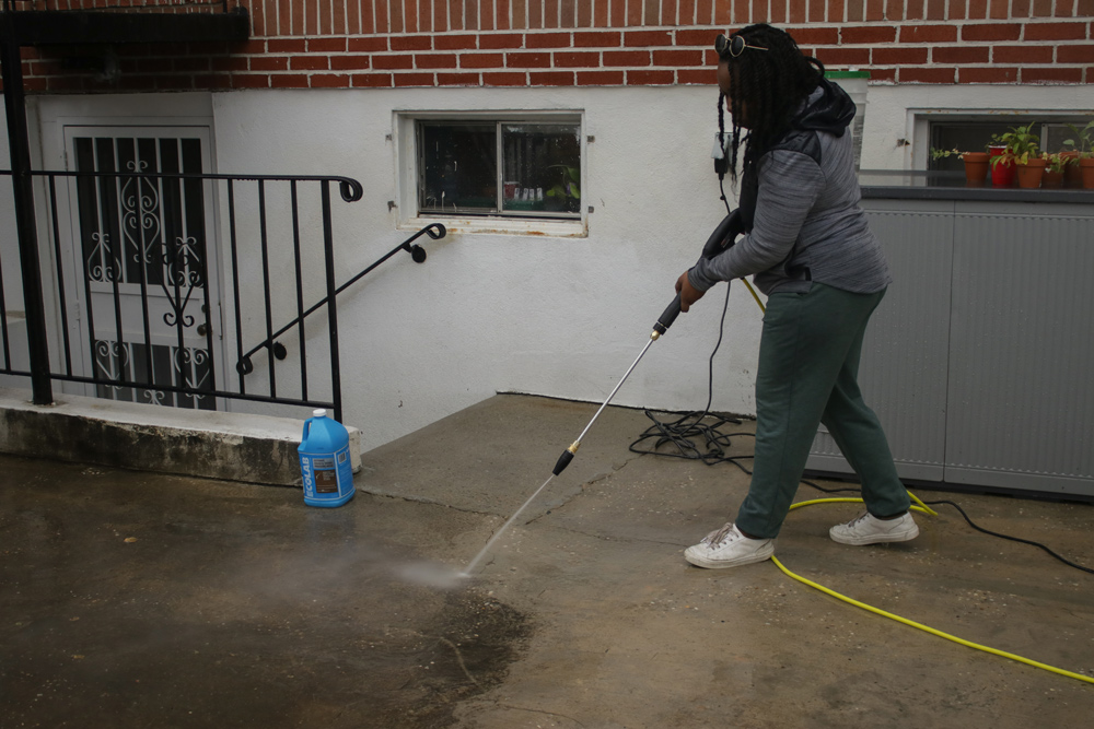 A woman pressure washing the concrete ground. 