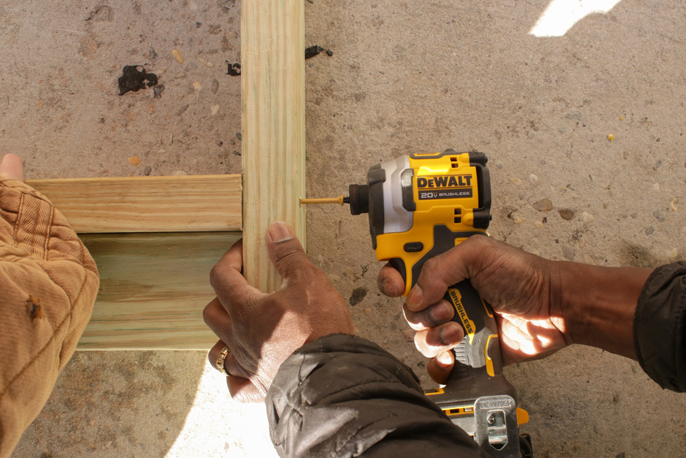A person using a Dewalt drill, while the other person holds the wood in place.
