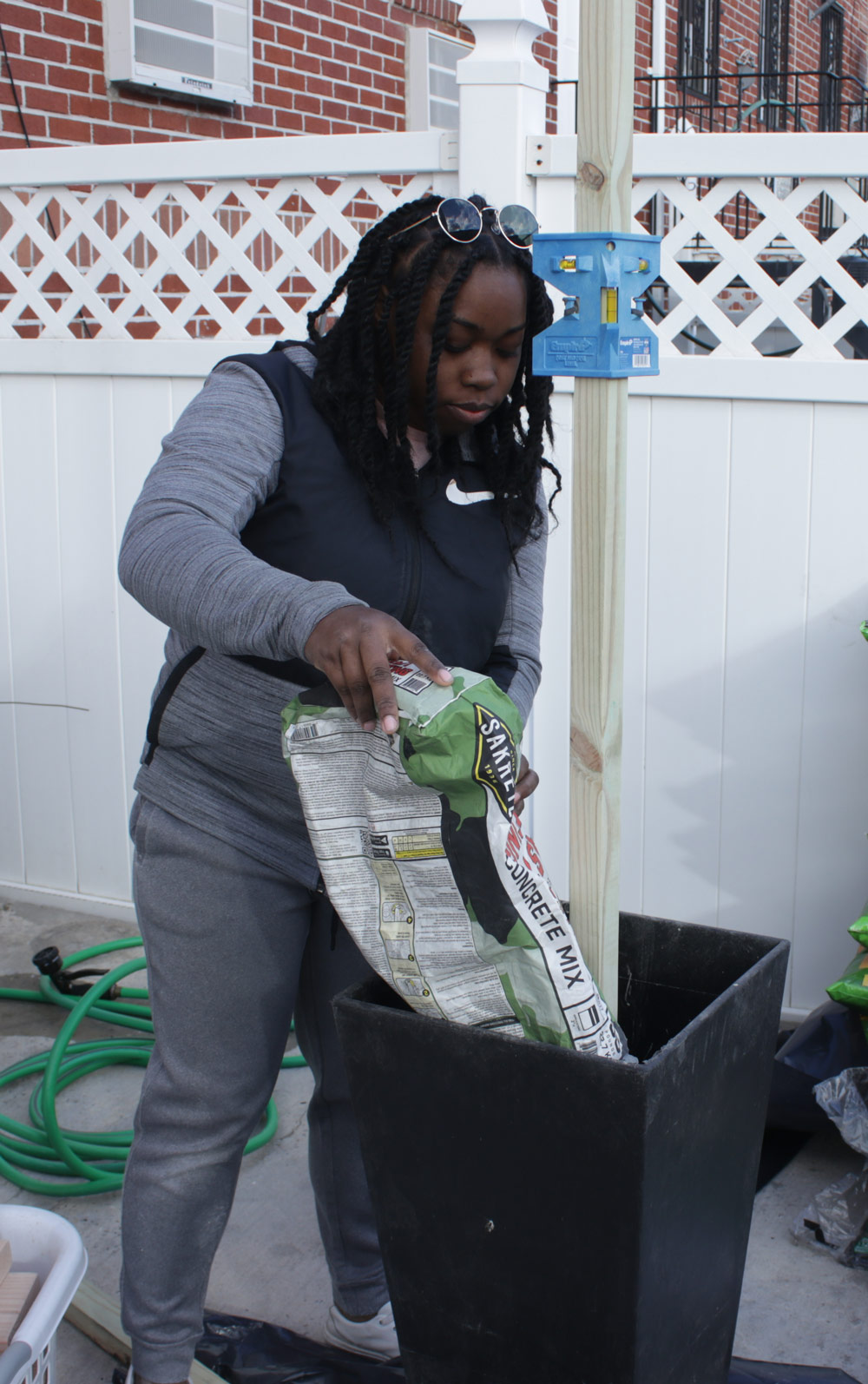 Woman adding 50-pound bags of concrete mix to a large black planter.