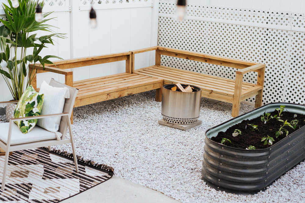 A wooden bench, fire pit, raised bed with plants, and patio set in the corner.