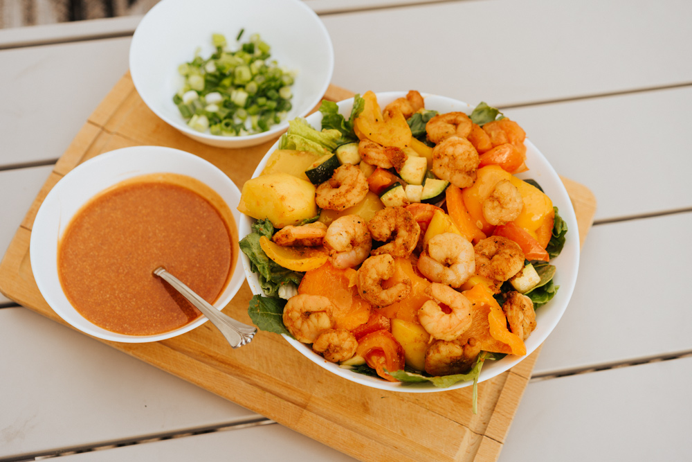 A shrimp salad dish on a cutting board with scallions and sauce on the side.
