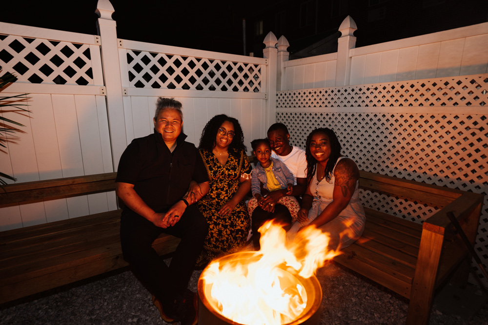 Three adults and two kids sitting in front of a fire pit at night.