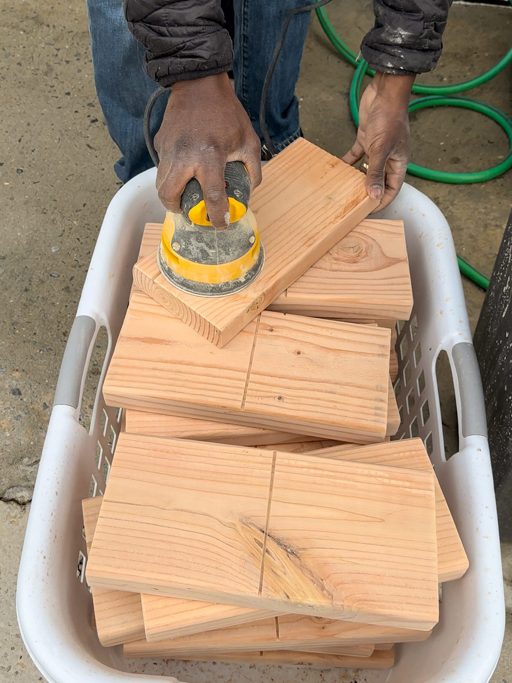 A person sanding wooden planks that are inside a basket. 