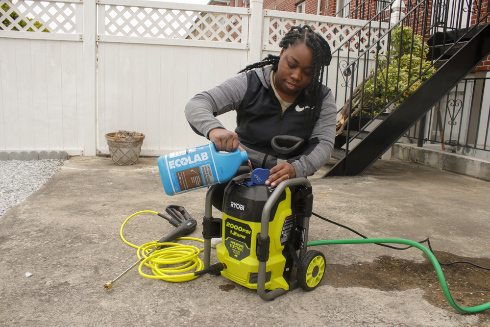 Woman pouring Ecolab wash into a pressure washing machine.