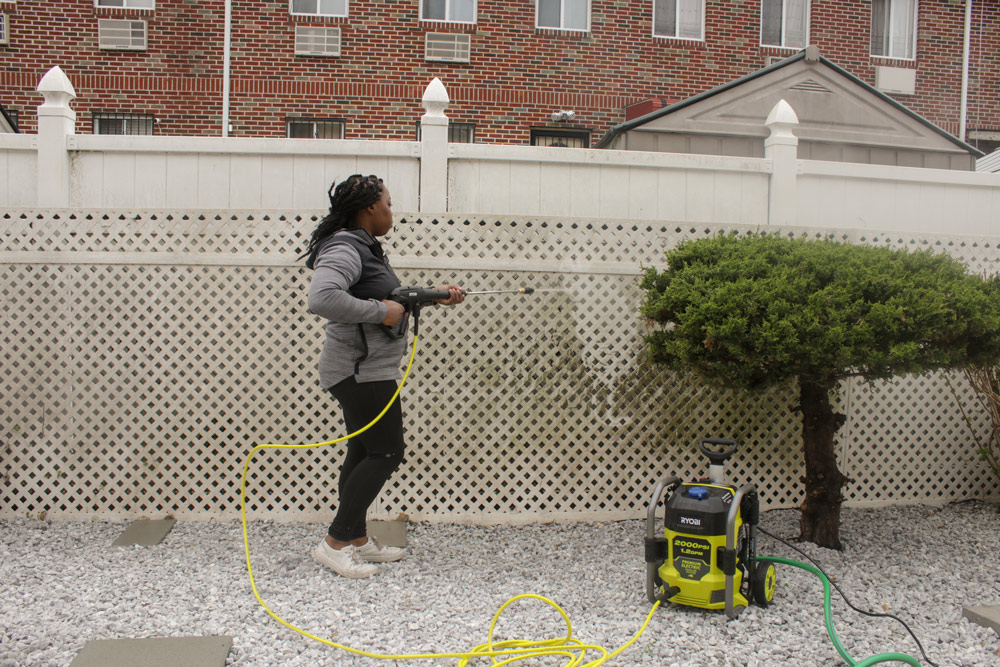 A woman pressure washing a dirty white fence.