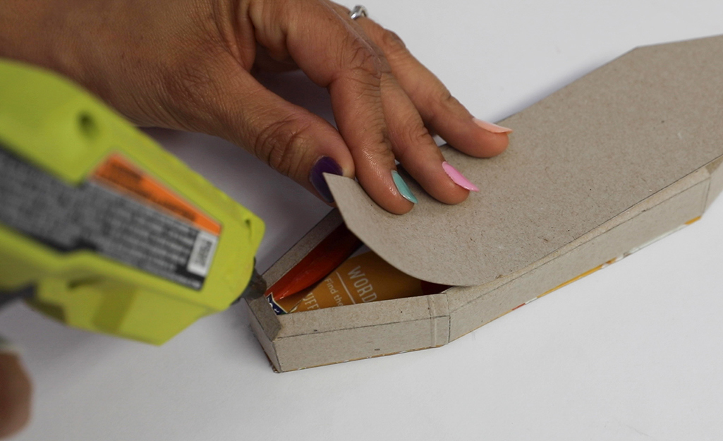 A person applying glue with a glue gun to a piece of cardboard.