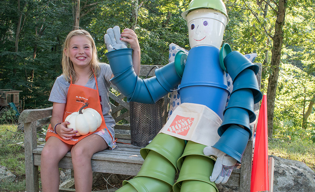 A child sitting with the flower pot scarecrow on an outdoor bench.