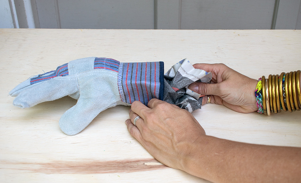 A person stuffing newspaper into a glove to make scarecrow hands.