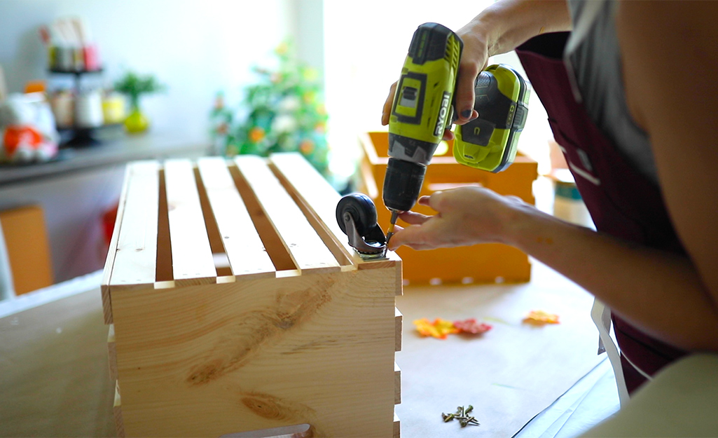 A person attaches wheels to a crate using a drill.