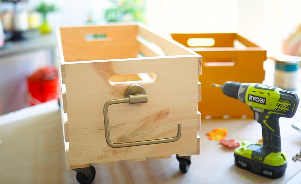 A crate with a towel ring displayed on a table alongside a drill.